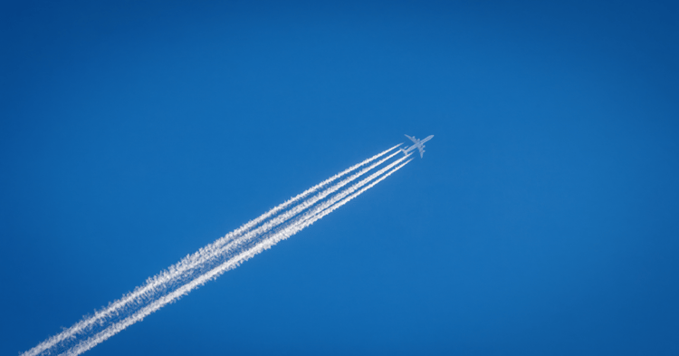 A commercial airplane flies diagonally across a clear blue sky, leaving four distinct white contrails behind it