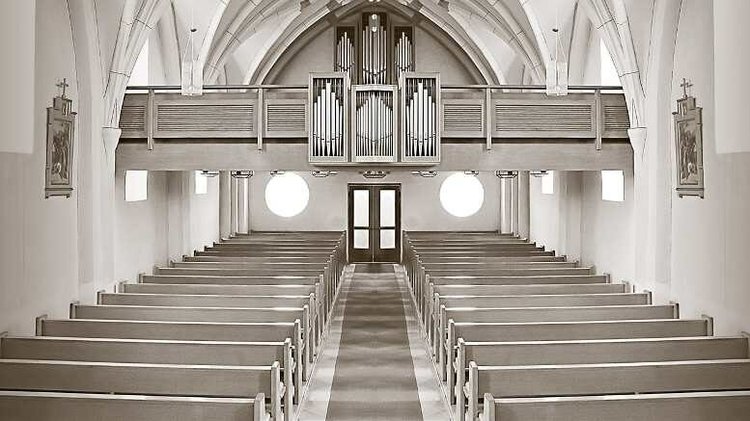 Interior view of a church sanctuary with rows of pews, an organ loft, and arched windows, reflecting the congregation’s fo...