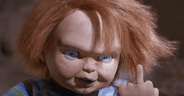 Chucky doll with orange hair and blue eyes pointing its middle finger