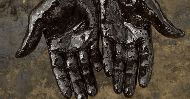 Two hands covered in thick black oil, palms facing upward against a rough surface