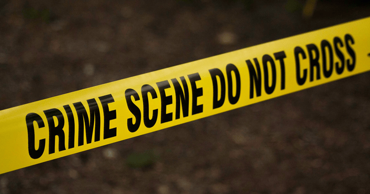 Yellow caution tape with black text reading CRIME SCENE DO NOT CROSS angled across a blurred ground background